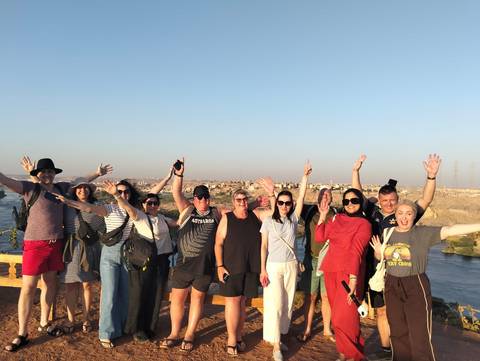 Cheerful tour group raising their arms at a riverside viewpoint under clear blue skies