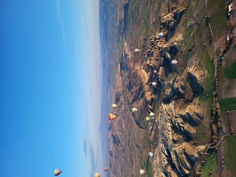 Sweeping aerial view of Cappadocian valleys dotted with colourful hot-air balloons at sunrise.