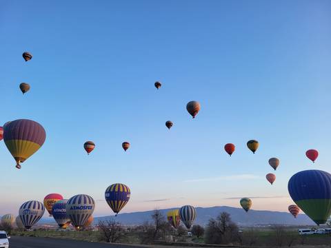 Dozens of colourful hot-air balloons drifting across a clear blue Cappadocia sky.