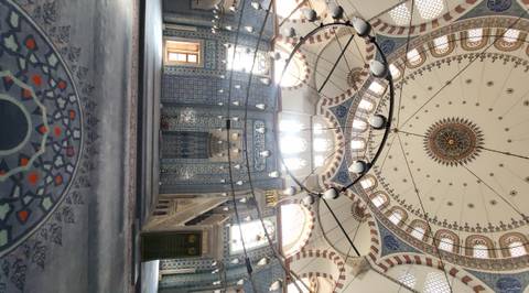 Intricately tiled interior of an Ottoman mosque with domed ceiling and patterned carpet lit by soft light.