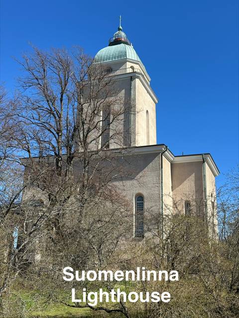 Light-coloured stone church tower partly hidden by leafless trees under a clear blue sky.