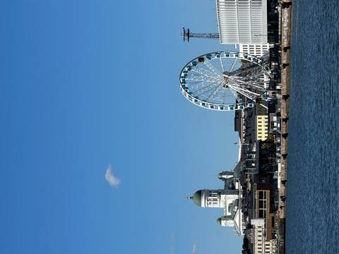City waterfront with Helsinki Cathedral dome and SkyWheel Ferris wheel rising above harbour buildings.