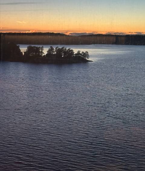 Wide expanse of tranquil lake water with a small tree-covered island at dusk.