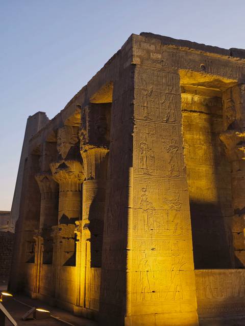 Night-lit Egyptian temple column covered in hieroglyphics glowing golden against surrounding dark stone walls.