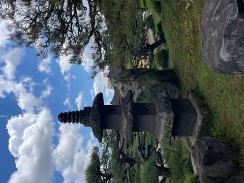 Stone pagoda and manicured pines in a traditional Japanese garden under blue skies with clouds.