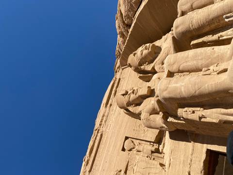 Massive carved sandstone statues of seated pharaohs rise against a cloudless deep-blue sky.