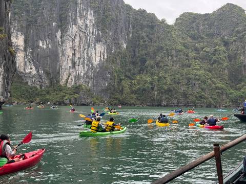 Dozens of colourful kayaks paddle on emerald waters beneath towering limestone walls.