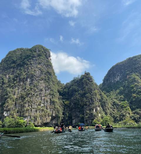 Steep green karst peaks rise against a blue sky dotted with soft white clouds.