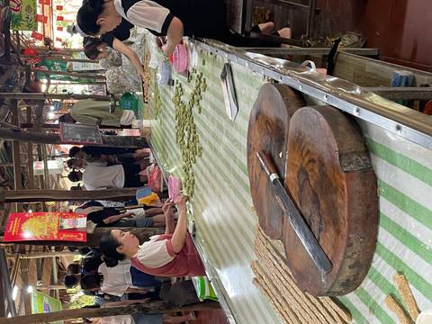 Local women prepare traditional sweets at long tables in a bustling rural market hall.