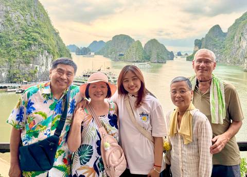 Family poses with smiling faces on a cruise deck overlooking the limestone towers of Halong Bay.