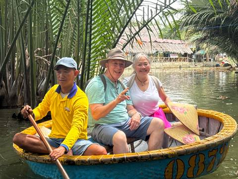 Tourists sit in a circular bamboo boat paddled through calm waters bordered by palms.