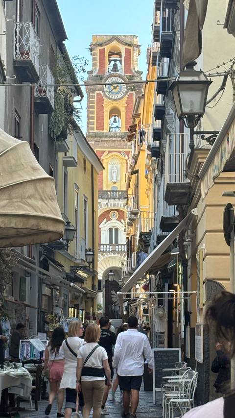 Narrow Italian alleyway framed by tall pastel buildings, revealing a distant church façade with statue.