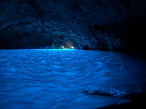 Glowing blue water fills a dark sea cave with light streaming from a distant entrance.