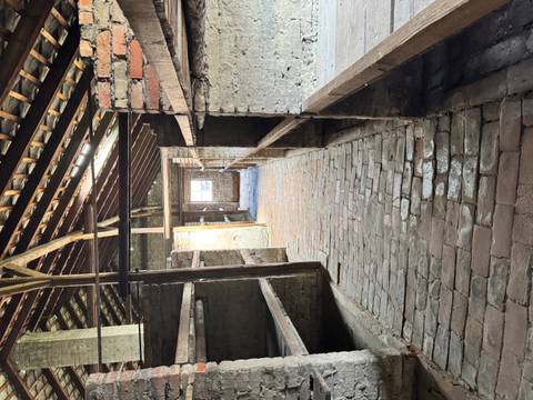 Long brick barrack interior with wooden three-tier bunks in rows under a timber roof.