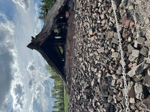 Rubble of a collapsed brick building behind a rope barrier under partly cloudy skies.