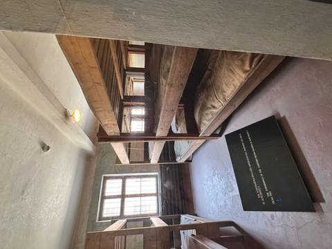 Wooden three-tier bunk beds inside a sparse dormitory room with barred windows.