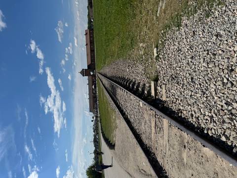 Railway tracks leading through the brick gatehouse of Birkenau under a bright blue sky.
