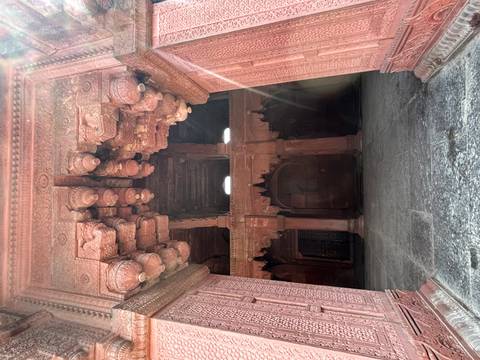 Red sandstone hall with ornate brackets and a shaft of sunlight inside a Mughal-era palace.