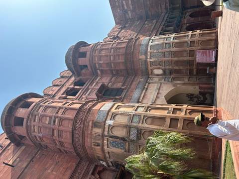 Massive red sandstone gateway tower of Agra Fort with a visitor standing in the sunlit forecourt.