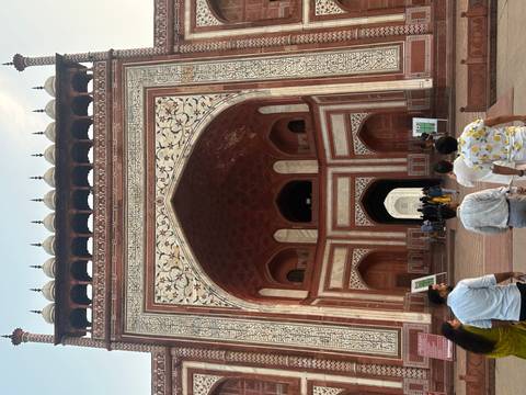 Marble-inlaid Mughal gateway leading into the Taj complex with visitors walking below.