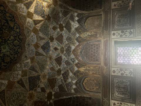 Intricate geometric and floral ceiling inside a historic Mughal palace, dimly lit by window light.