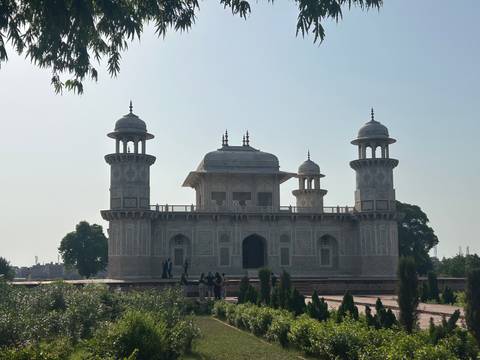 Silhouetted marble tomb of Itimad-ud-Daulah with small groups of visitors against a bright sky.