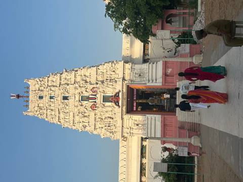White Hindu temple gopuram richly carved, with visitors ascending the entrance steps under a clear sky.