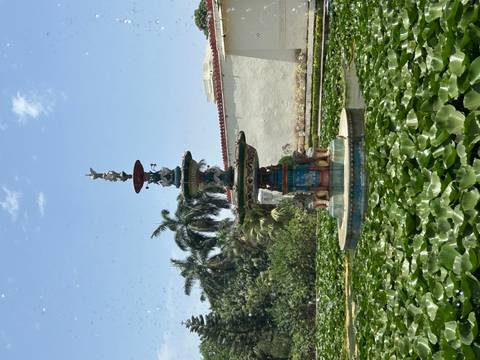 Colorful tiered fountain surrounded by lily pads in a sunny courtyard with palm trees.