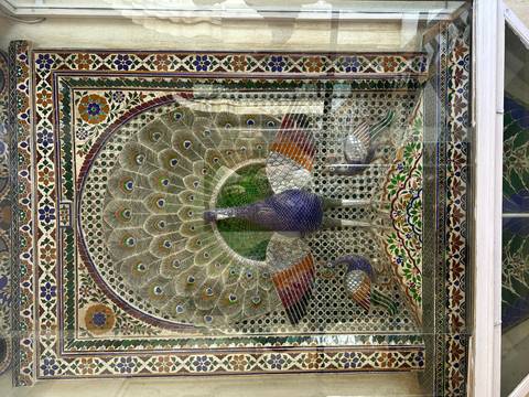 Colorful glass and tile mosaic of a peacock displayed inside a palace window alcove.