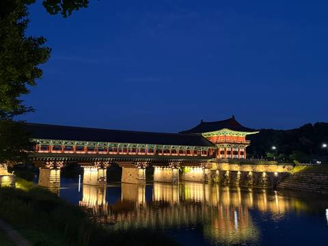 Illuminated traditional covered bridge reflecting in calm river at night