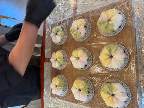Tray of colorful rice cakes being prepared, with gloved hands arranging the sweets