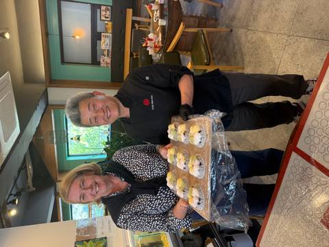 Two smiling participants proudly holding a tray of freshly made rice cakes in a workshop