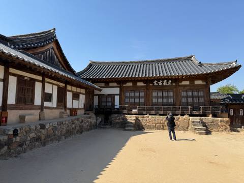 Traditional wooden hanok courtyard with a visitor taking photos under clear skies