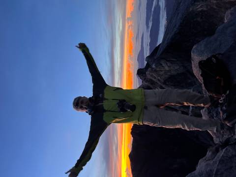 Triumphant climber on a rocky summit silhouetted against a vivid sunrise sky.