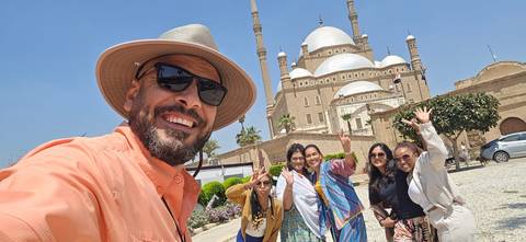 Selfie of smiling guide and group waving in front of the domes and minarets of the Mosque of Muhammad Ali.