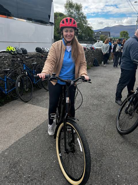 Young woman smiles while holding an e-bike in a paved courtyard surrounded by other bicycles