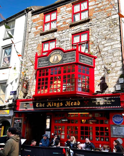 Bright red timber façade of The Kings Head pub stands out against a grey stone street in Galway