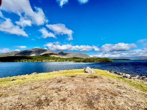 Crystal clear lake bordered by rolling hills and distant mountains under a vibrant blue sky