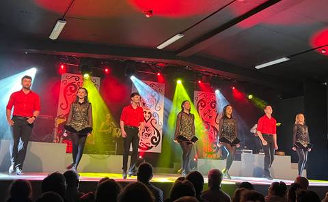 Lively Irish dance troupe performs on a brightly lit stage in coordinated red and black costumes