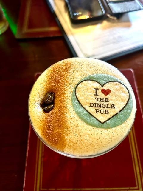 Close-up of a frothy coffee with printed heart graphic reading 'I love The Dingle Pub' beside roasted coffee beans