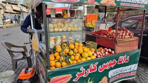 A street juice cart displays fresh oranges, pomegranates and cups while the vendor prepares drinks.