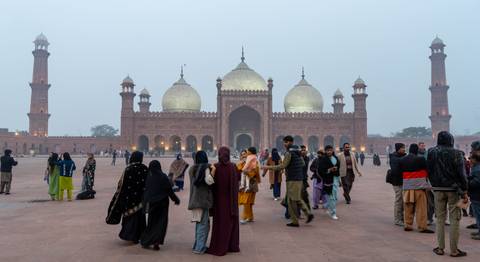 Misty morning scene of Badshahi Mosque with visitors walking across its vast courtyard.