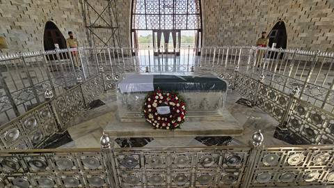 Marble sarcophagus draped in a Pakistani flag is displayed behind silver railings inside a mausoleum.