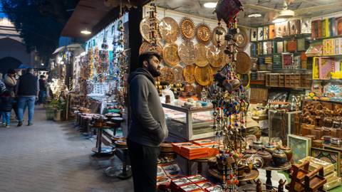 An evening bazaar alley lined with handicraft stalls and hanging ornaments as a man browses.