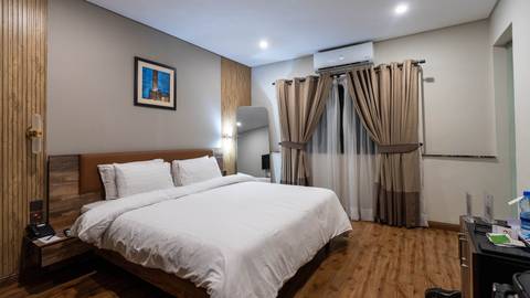 Modern hotel room with a neatly made double bed, wooden floor, neutral decor and soft lighting.