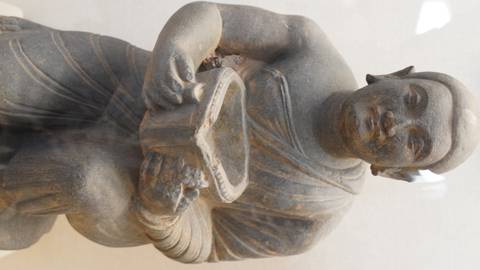 Stone sculpture of a kneeling ancient figure inside a museum display case.