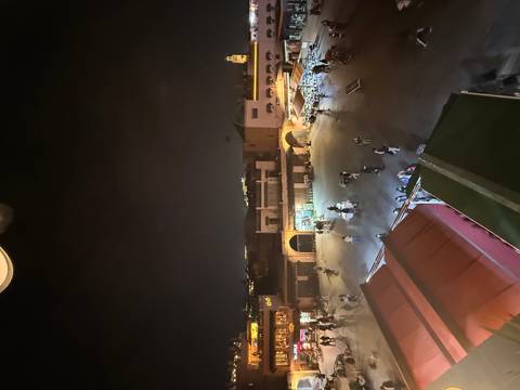 Nighttime overhead view of Jemaa el-Fnaa square with scattered shoppers and glowing shop lights.