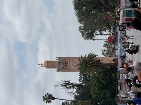 The Koutoubia Mosque minaret rises above palm trees and bustling crowds in Marrakesh.