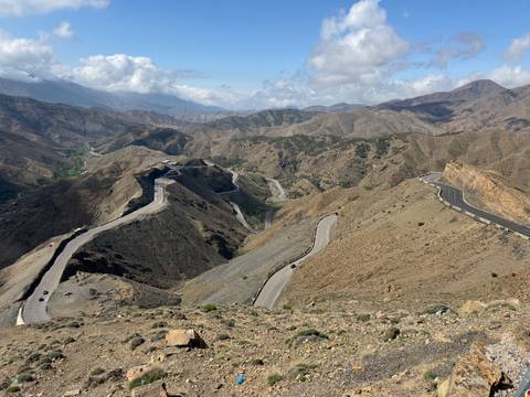 Panoramic view of winding mountain roads cutting across rugged Atlas peaks under a bright sky.