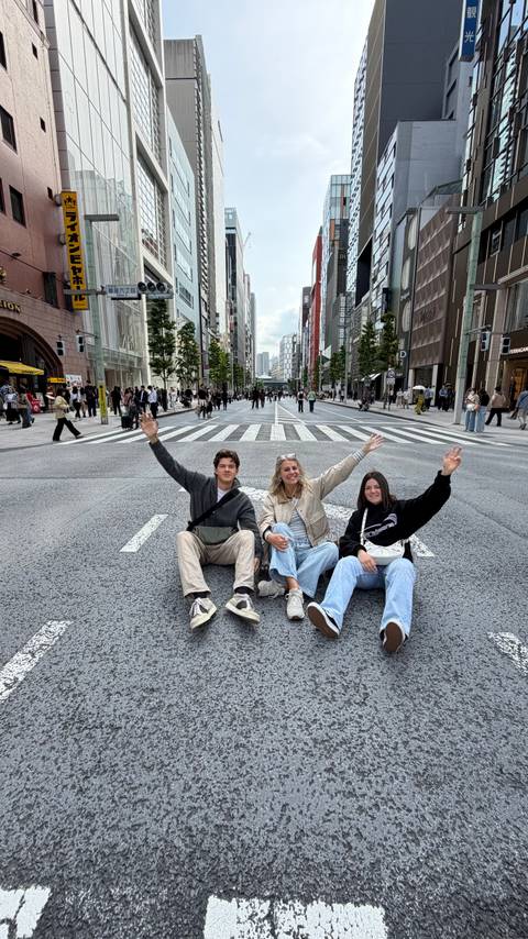 Three travellers sitting in the middle of a closed Tokyo street waving cheerfully